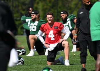 Brady Cook, wearing a red jersey with number 4, stretches during practice.