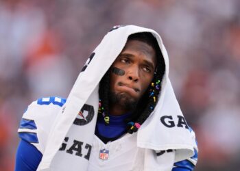 CeeDee Lamb in a white Dallas Cowboys jersey with a towel over his head, walking along the sideline during a game.
