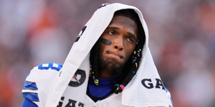 CeeDee Lamb in a white Dallas Cowboys jersey with a towel over his head, walking along the sideline during a game.