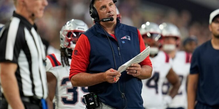 A football coach wearing a headset and Patriots vest reviews game strategy.