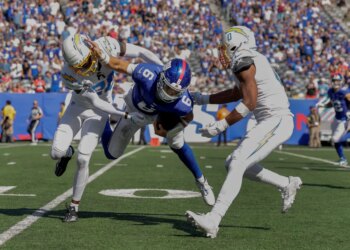Giants quarterback Jaxson Dart (6) is tackled by Los Angeles Chargers cornerback Cam Hart (20) and linebacker Daiyan Henley (0) during the third quarter on Sept. 28, 2025.