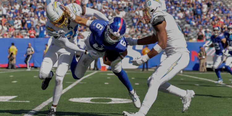 Giants quarterback Jaxson Dart (6) is tackled by Los Angeles Chargers cornerback Cam Hart (20) and linebacker Daiyan Henley (0) during the third quarter on Sept. 28, 2025.