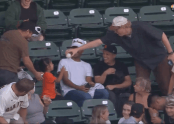 A baseball player hands a baseball to a young girl in the stands.