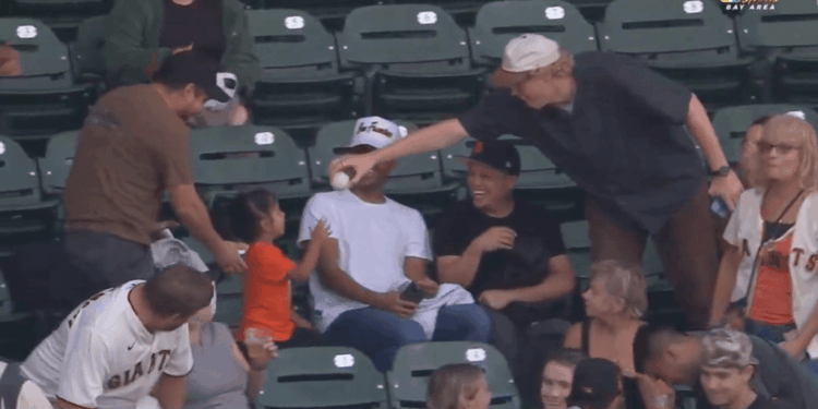 A baseball player hands a baseball to a young girl in the stands.