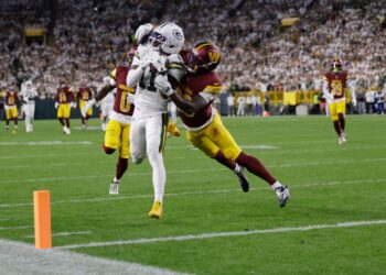 Green Bay Packers receiver making a catch while defended by Washington Commanders players.