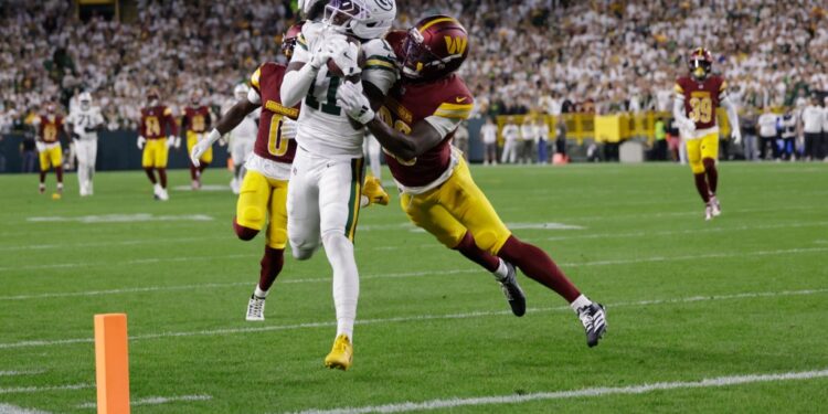 Green Bay Packers receiver making a catch while defended by Washington Commanders players.
