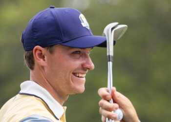 Ludvig Aberg smiling while holding golf clubs.