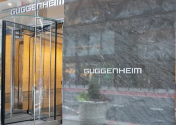 Guggenheim Partners logo on a marble wall next to a revolving glass door.