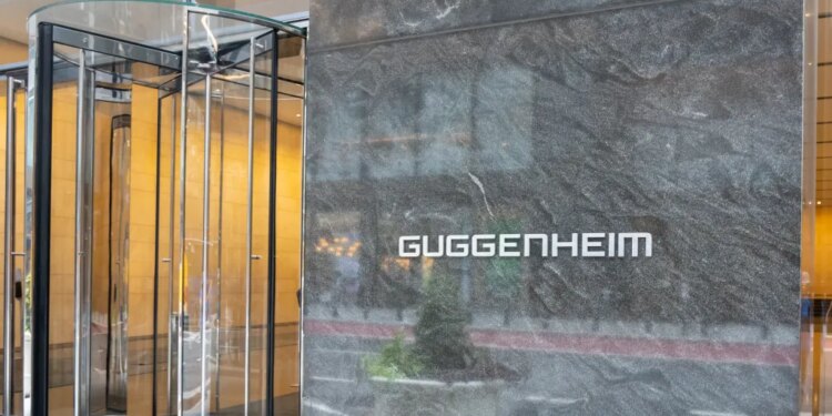 Guggenheim Partners logo on a marble wall next to a revolving glass door.