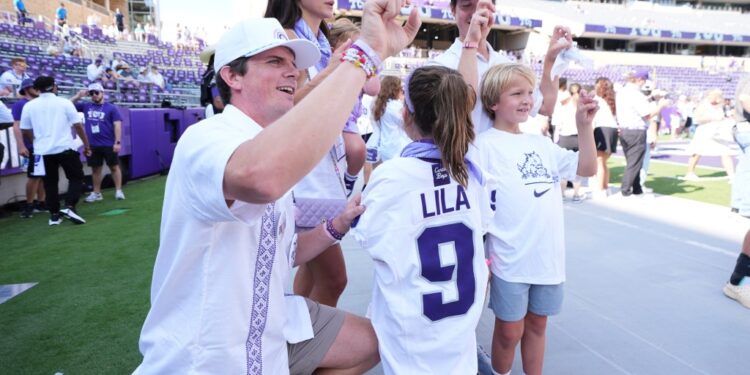 Blake Bonner, his wife Caitlin, and their children, with one daughter wearing a shirt with her late sister's name, on the field before a college football game.