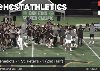 Soccer players and coaches on a green field with a "Dan Finn Soccer Classic" banner and a score overlay showing "St. Benedicts - 1 St. Peter's - 1 (2nd Half)".