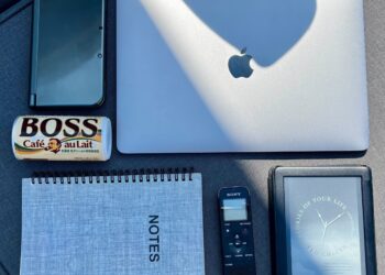 A photo of a laptop, Nintendo 3DS, Kindle, notebook, voice recorder, and can of Boss coffee.