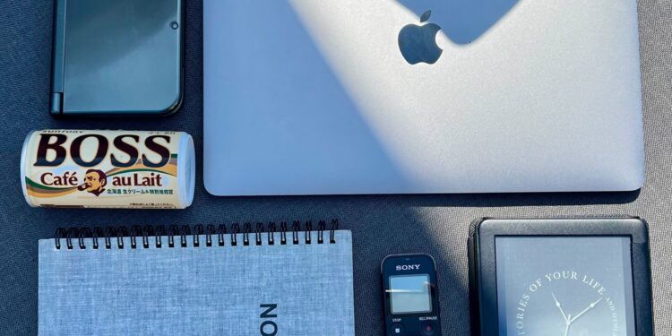 A photo of a laptop, Nintendo 3DS, Kindle, notebook, voice recorder, and can of Boss coffee.