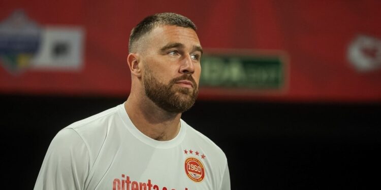 Travis Kelce wearing a white shirt with a Kansas City Chiefs emblem.