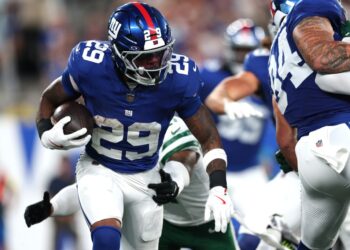 New York Giants player running with the football during a preseason game.