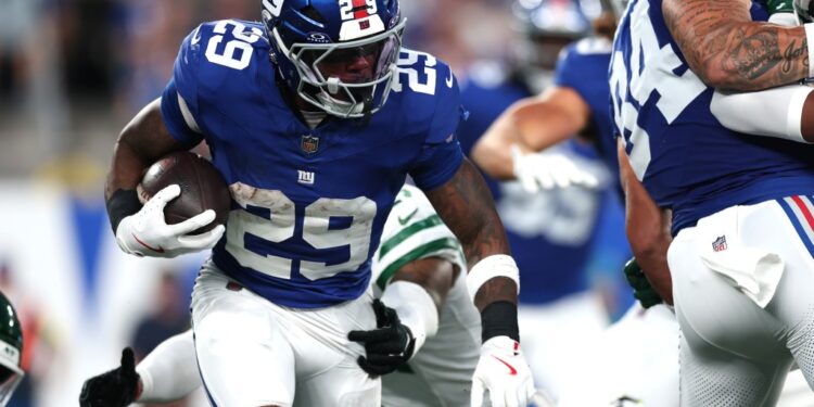 New York Giants player running with the football during a preseason game.