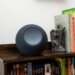 The 2025 Amazon Echo Studio sitting on a wooden shelf next to a collection of books, with a white wall behind it.