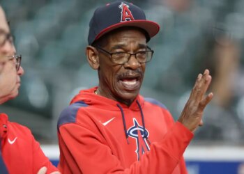 Angels fan in an Angels cap and hoodie, speaking with open mouth, with another person to his left.