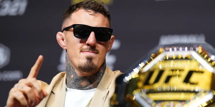 Tom Aspinall wearing sunglasses and a gold chain, pointing his finger with a UFC belt in the foreground.