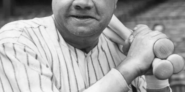 Babe Ruth holding warm-up bats in his baseball uniform.