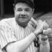 Babe Ruth holding warm-up bats in his baseball uniform.