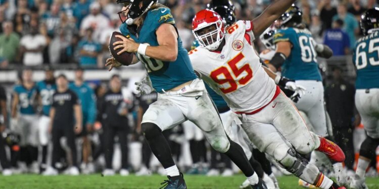 Jacksonville Jaguars quarterback Trevor Lawrence (16) running with the ball as Kansas City Chiefs defensive tackle Chris Jones (95) attempts to tackle him.