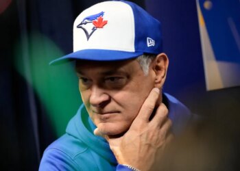 Don Mattingly wearing a blue and white Toronto Blue Jays baseball cap, holding his chin.