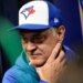 Don Mattingly wearing a blue and white Toronto Blue Jays baseball cap, holding his chin.