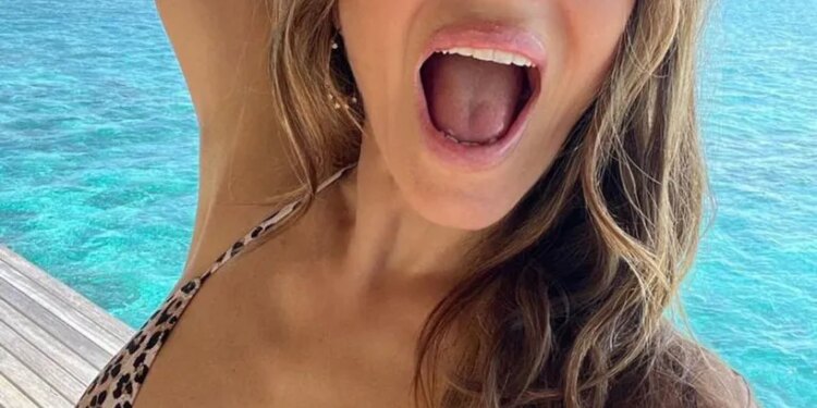 A woman in a leopard print bikini top taking a selfie with a surprised expression by turquoise water.