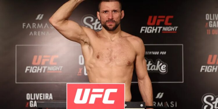A man stands shirtless on a scale, flexing his right arm at the UFC Fight Night weigh-in.