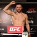 A man stands shirtless on a scale, flexing his right arm at the UFC Fight Night weigh-in.