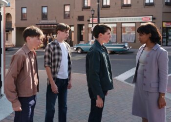 A black woman in a lilac skirt with matching jacket. The women is speaking sternly to three white teenaged boys on a street corner.