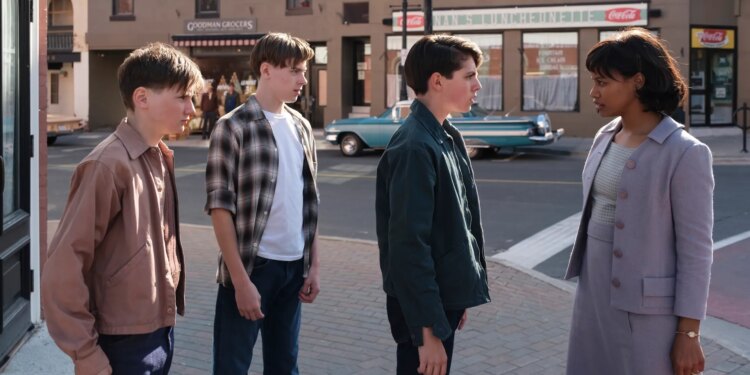 A black woman in a lilac skirt with matching jacket. The women is speaking sternly to three white teenaged boys on a street corner.