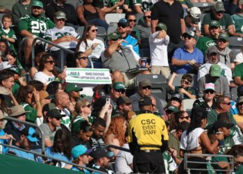 New York Jets fans in the stands, with one fan holding a sign that reads "Rare Footage: Optimistic Jets Fans."