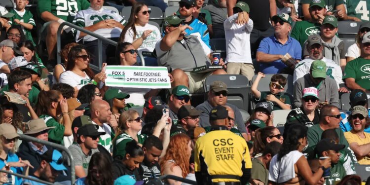 New York Jets fans in the stands, with one fan holding a sign that reads "Rare Footage: Optimistic Jets Fans."