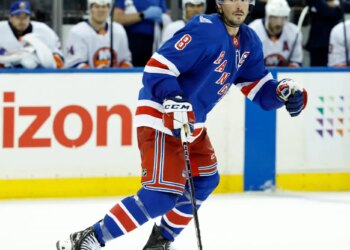 J.T. Miller of the New York Rangers skating on ice in front of the New York Islanders bench.
