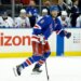 J.T. Miller of the New York Rangers skating on ice in front of the New York Islanders bench.