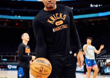 Ike Azotam wearing a black "Knicks Basketball" shirt and holding a Wilson basketball on a court.