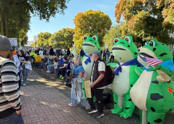 Protesters pose for photos with a trio of inflatable frogs at the October No Kings protest in downtown Portland.