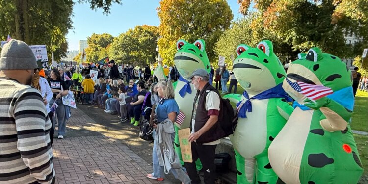 Protesters pose for photos with a trio of inflatable frogs at the October No Kings protest in downtown Portland.