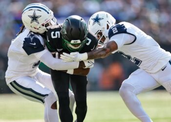 Two Dallas Cowboys players tackle a New York Jets player.