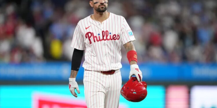 Philadelphia Phillies baseball player wearing a white pinstripe jersey with "Phillies" in red script, black eye black, and holding a red helmet.