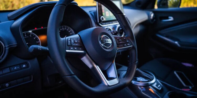 Interior of a Nissan Juke, showing the steering wheel with the Nissan logo, dashboard, and infotainment screen.