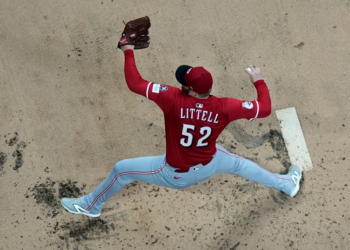 Baseball player Littell, number 52, wearing a red jersey, light gray pants, and a red cap, makes a throw from the pitcher's mound.