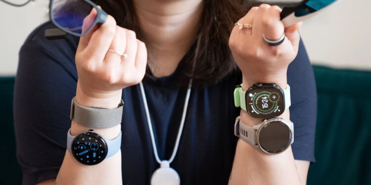 Close up of Senior reviewer Victoria Song holding two pairs of smart glasses, wearing four wrist-based wearables, a smart ring, and the Friend AI necklace.