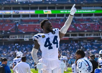 Indianapolis Colts linebacker Zaire Franklin points his finger up while standing on the sideline of a football field.