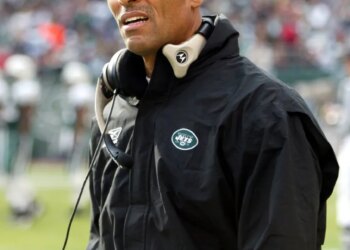 Herm Edwards, coach of the New York Jets, wearing a green cap and black jacket with a Jets logo.