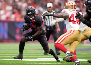 A Houston Texans player running with the football away from a San Francisco 49ers player.