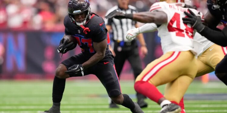 A Houston Texans player running with the football away from a San Francisco 49ers player.
