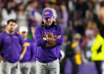 LSU head coach Brian Kelly standing on the sideline with his arms crossed.